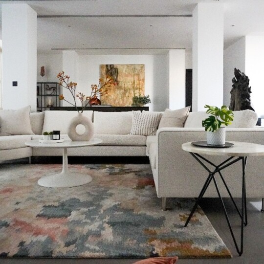 Elegant living room design by Roberts Renovations featuring a neutral corner sofa, textured rug, and modern art accents creating a warm, inviting atmosphere.